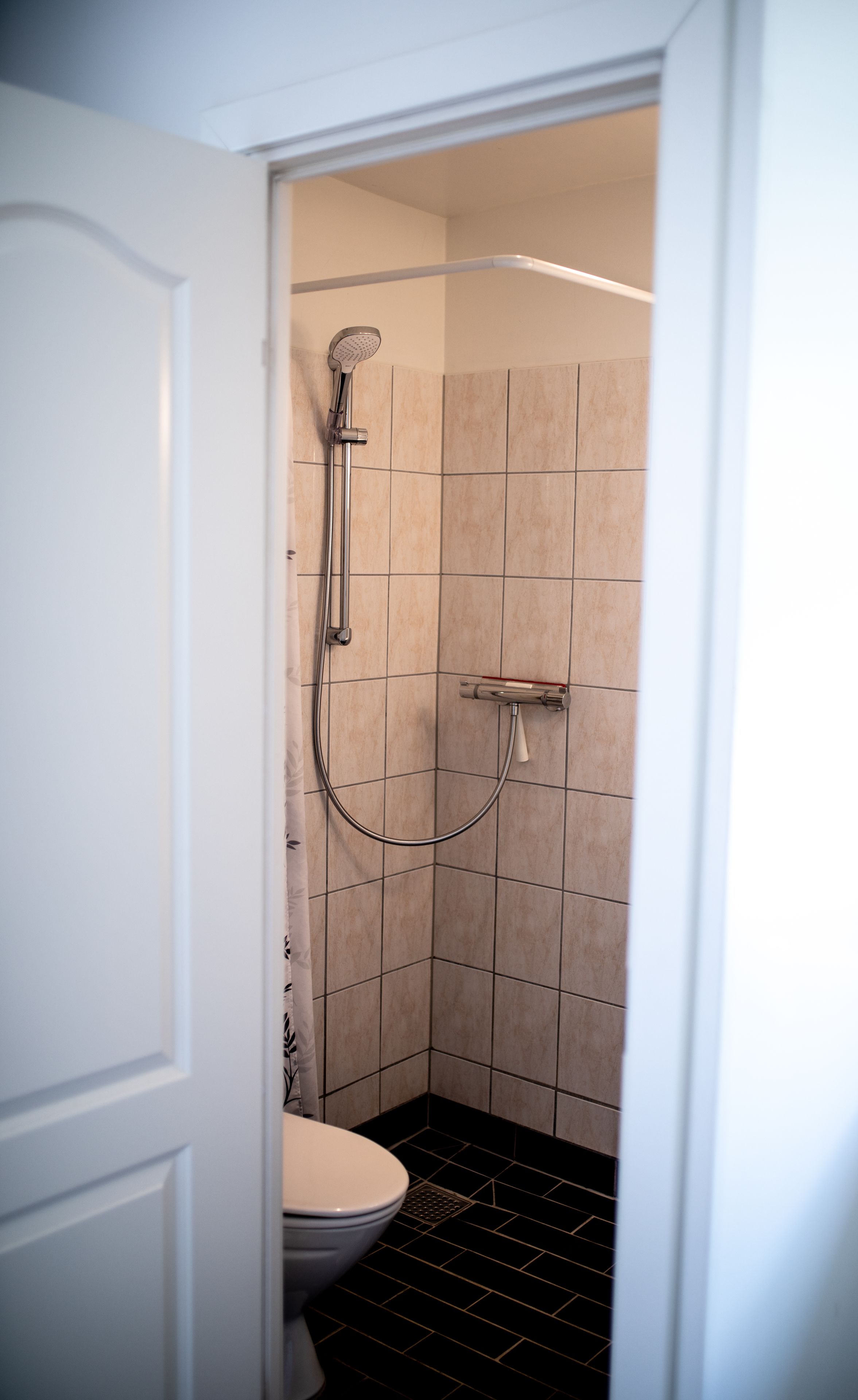 A small, modern bathroom with a toilet, a shower with a handheld showerhead, and tiled walls.