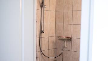 A small, modern bathroom with a toilet, a shower with a handheld showerhead, and tiled walls.