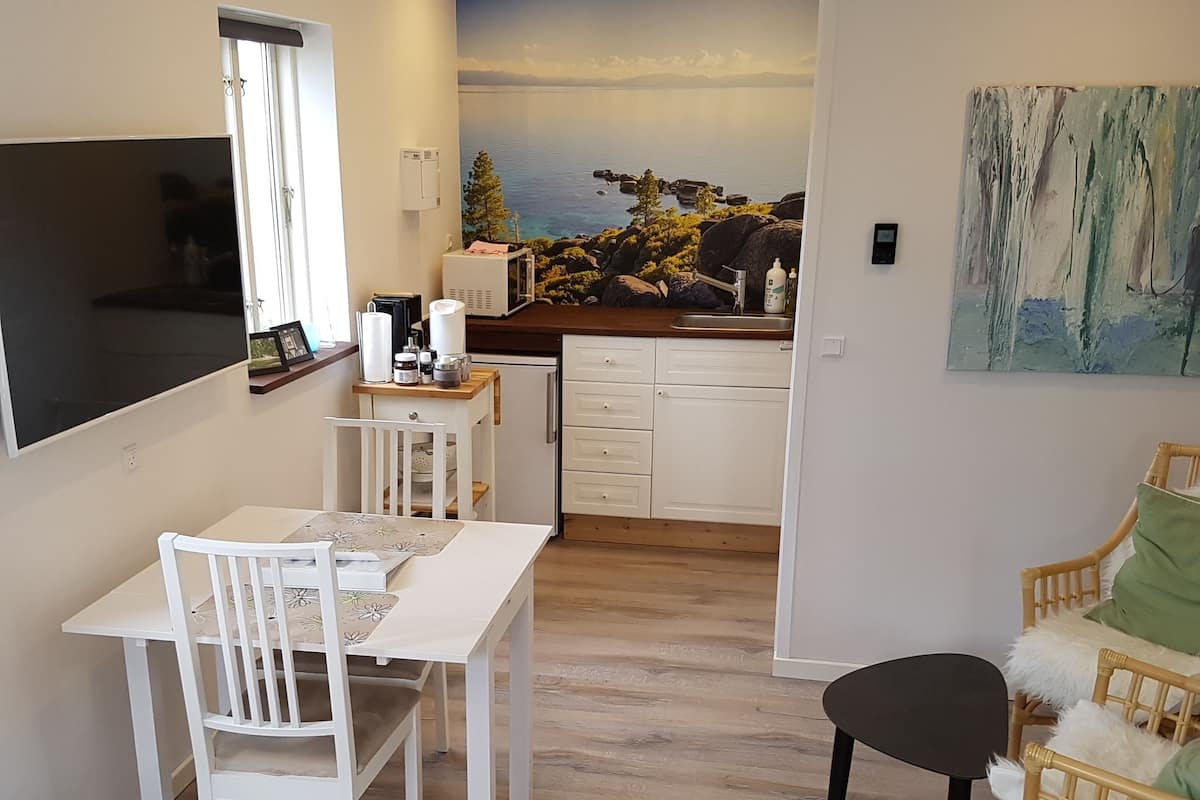 A modern kitchen with a scenic mural, a dining area with white furniture, and a cozy seating area with a wicker chair.