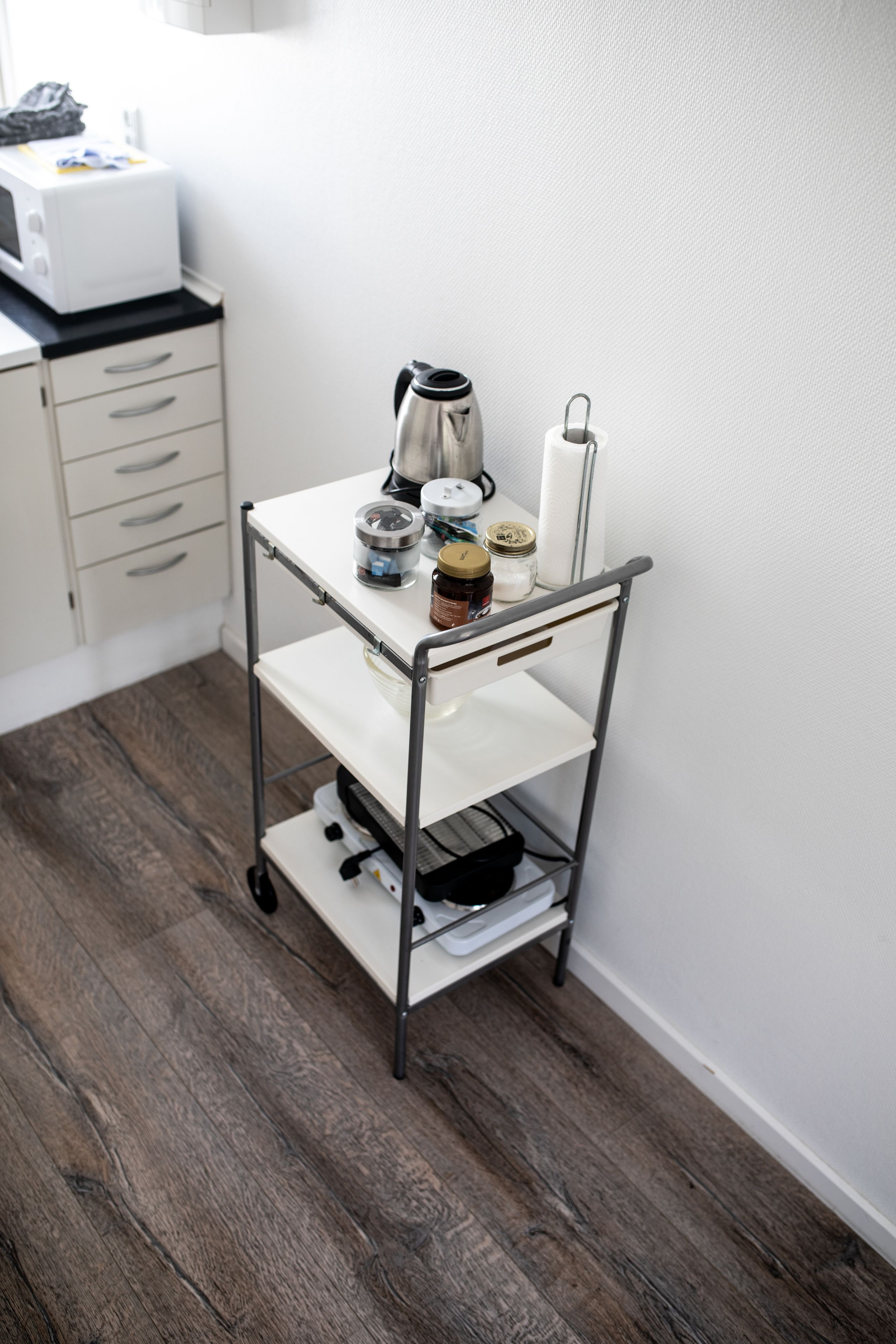 A kitchen area with a white countertop, a stainless steel coffee maker, a jar of honey, a roll of paper towels, and a white appliance.