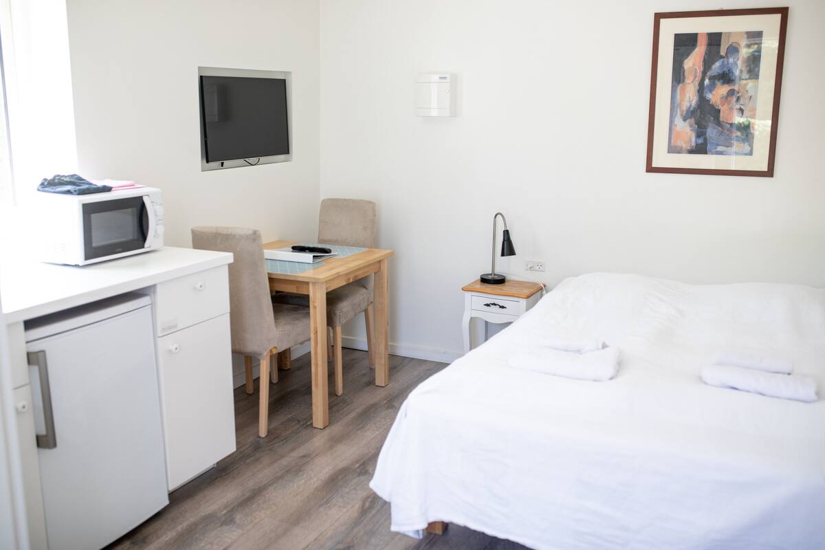 A hotel room with a bed, a desk with a chair, a microwave, a television, and a painting on the wall.