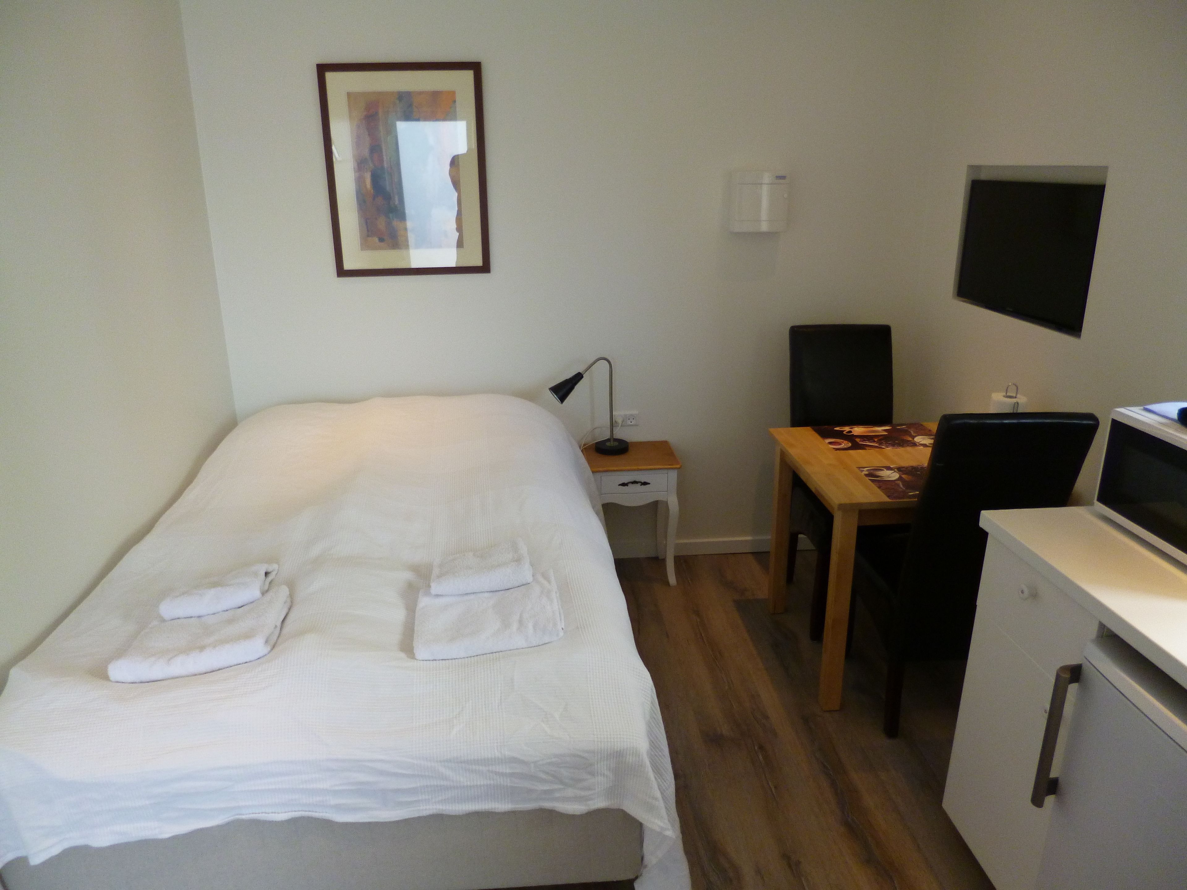 A neatly arranged bedroom with a bed, a desk, a chair, and a TV.