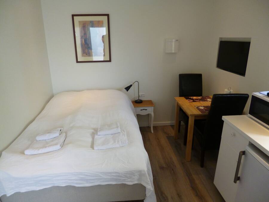 A neatly arranged bedroom with a bed, a desk, a chair, and a TV.