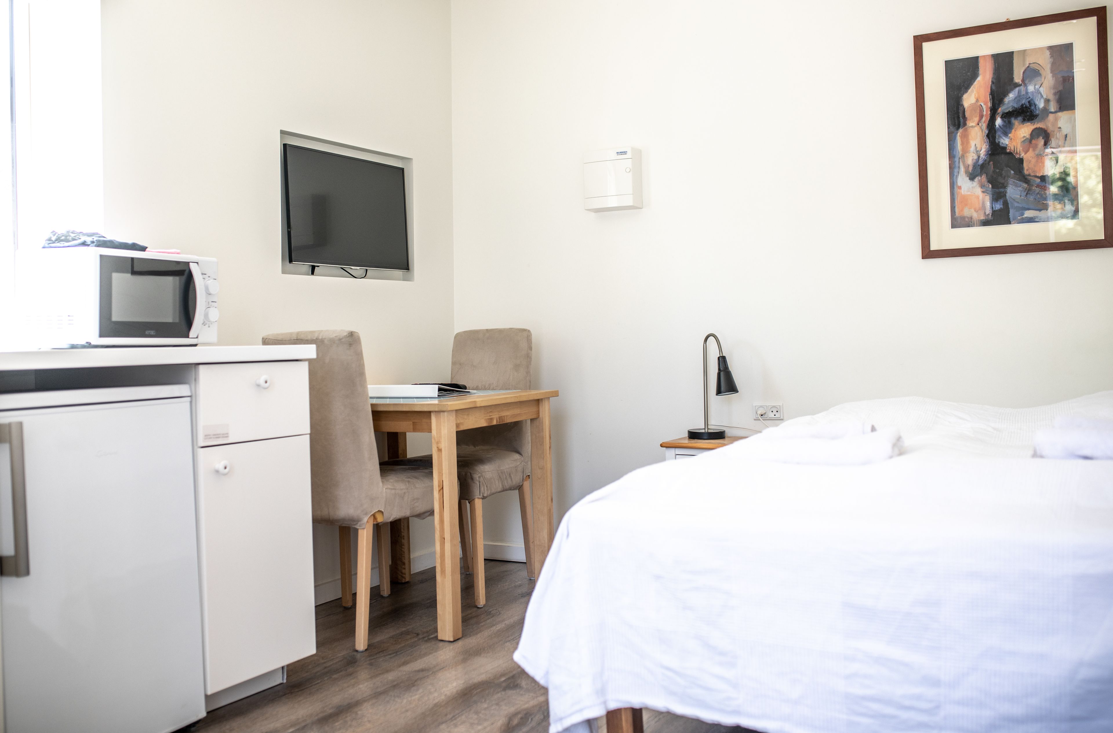A hotel room with a bed, a desk with a chair, a television, a microwave, and a painting on the wall.