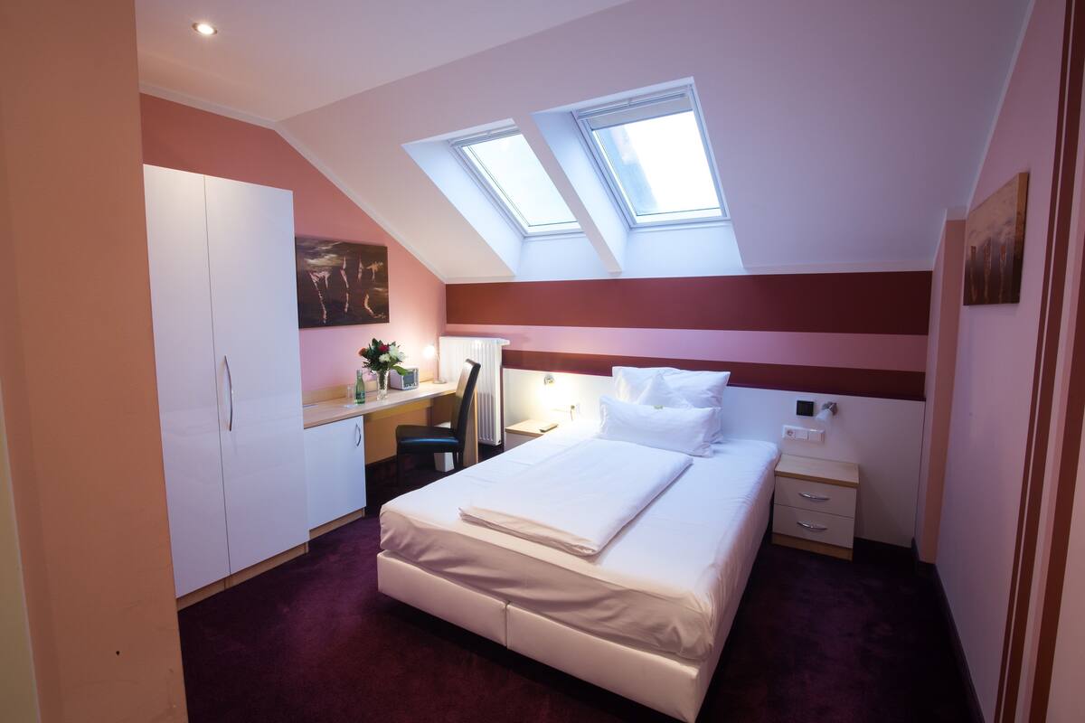 A bedroom with a bed, desk, chair, and skylights.