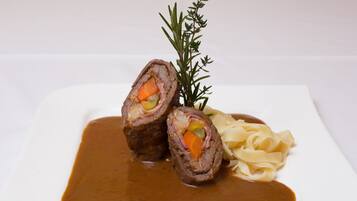 A plate with rolled meat, vegetables, and pasta, garnished with a sprig of rosemary.