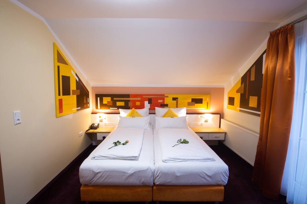 A hotel room with two beds, a nightstand with a phone, and a wall with geometric patterns.