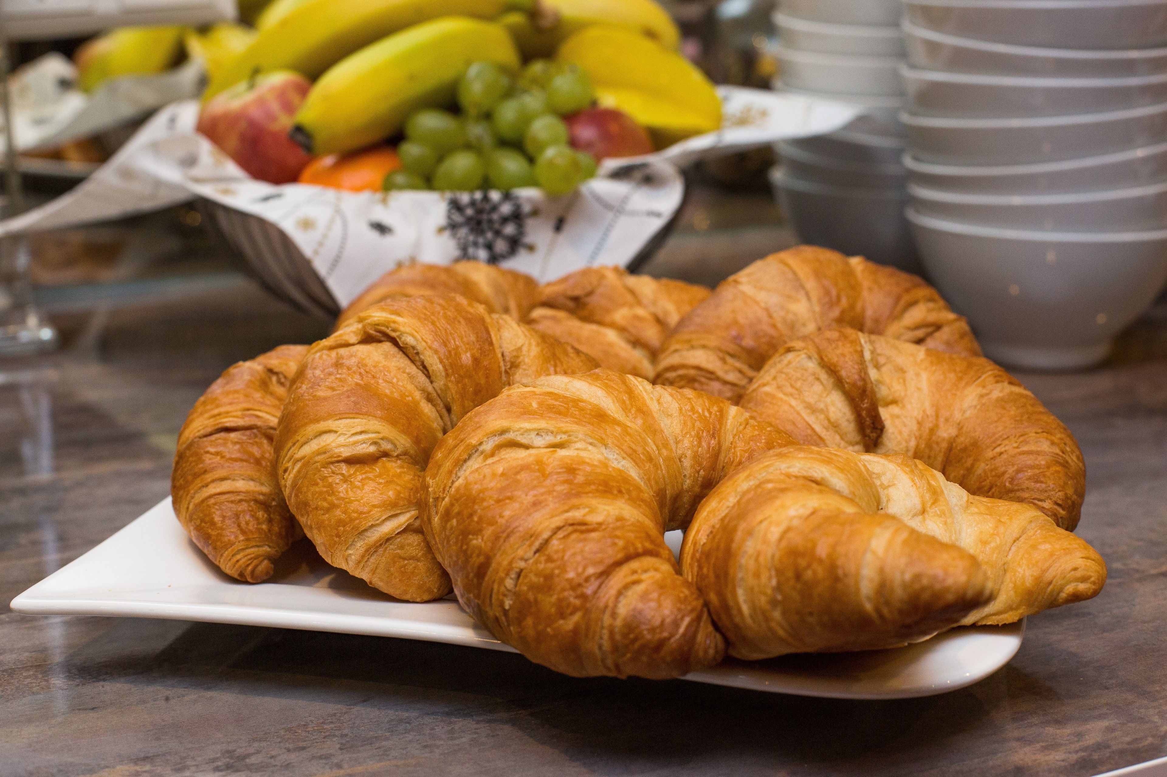 Ein Teller mit Croissants auf einer Marmorarbeitsplatte, im Hintergrund eine Obstschale.