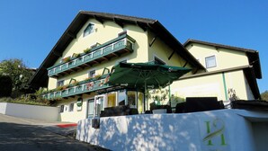Ein zweistöckiges Hotel mit grünem Balkon, Außenbereich zum Sitzen und einem Schild, das es als Hotel kennzeichnet.
