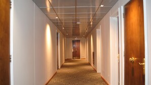 A corridor with wooden doors, white walls, and a patterned carpet. - Hotel Santa Lucia (Santiago)