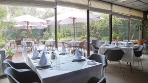 An outdoor dining area with tables set for two, covered by umbrellas, and surrounded by potted plants. - Hotel Santa Lucia (Santiago)