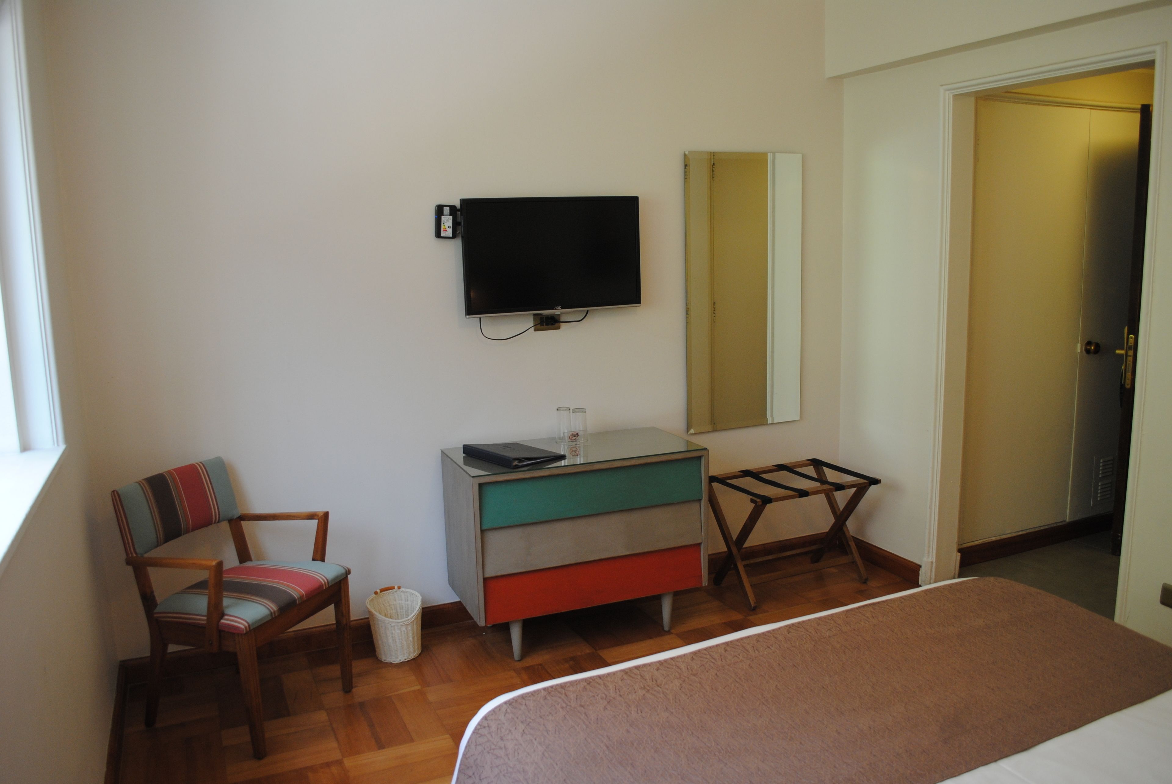 A bedroom with a bed, a chair, a dresser, a television, and a mirror.