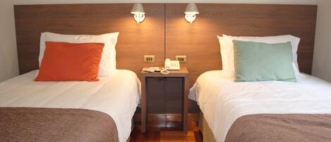 A hotel room with two beds, each with a pillow and a bedside table with a lamp.