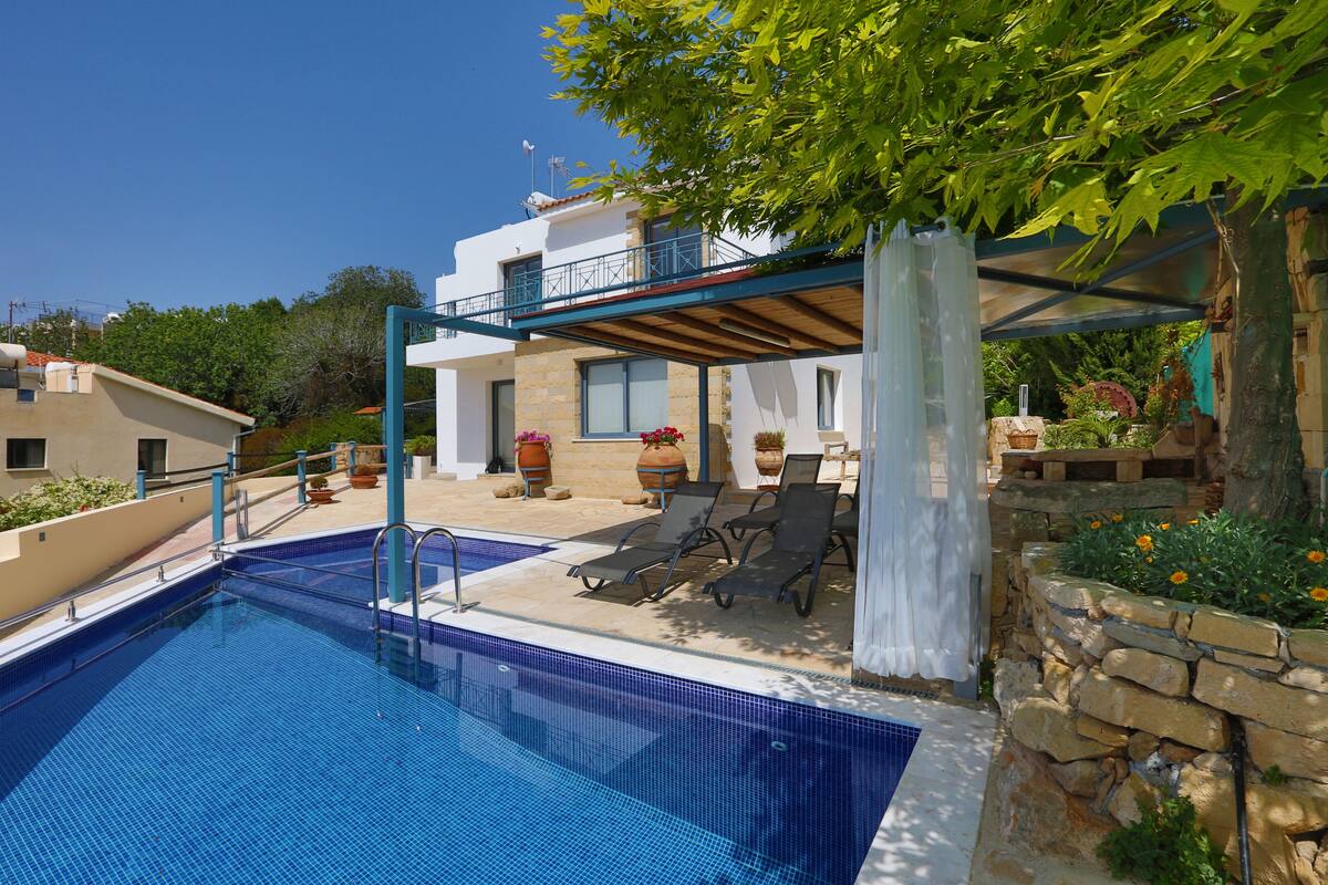 A swimming pool with lounge chairs, a covered patio, and a stone wall with flowers.