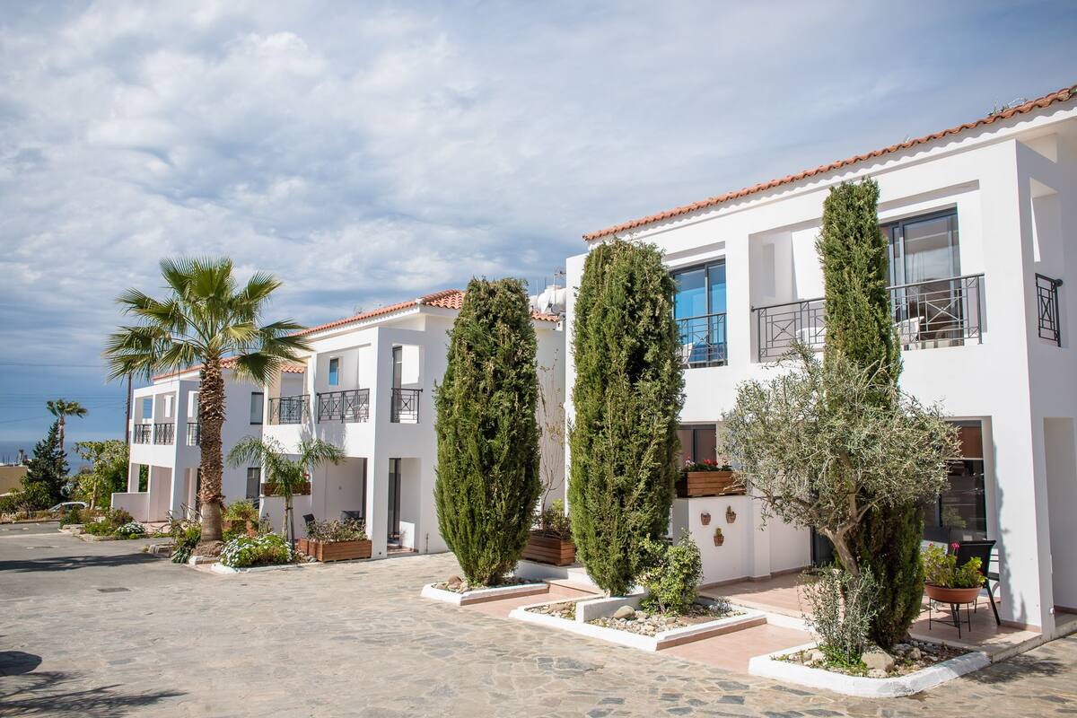 A modern building with white walls and red-tiled roofs, featuring balconies and potted plants.