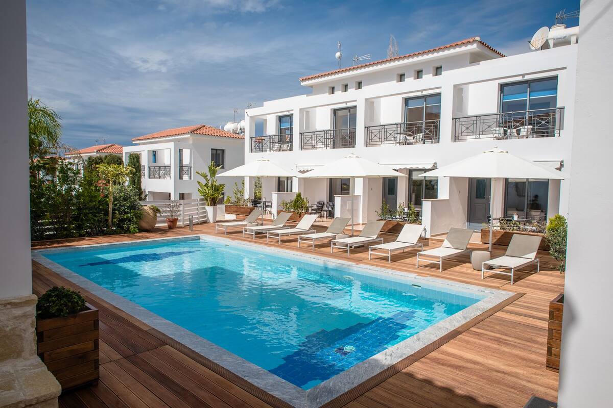 A modern hotel with a swimming pool, sun loungers, and outdoor seating.