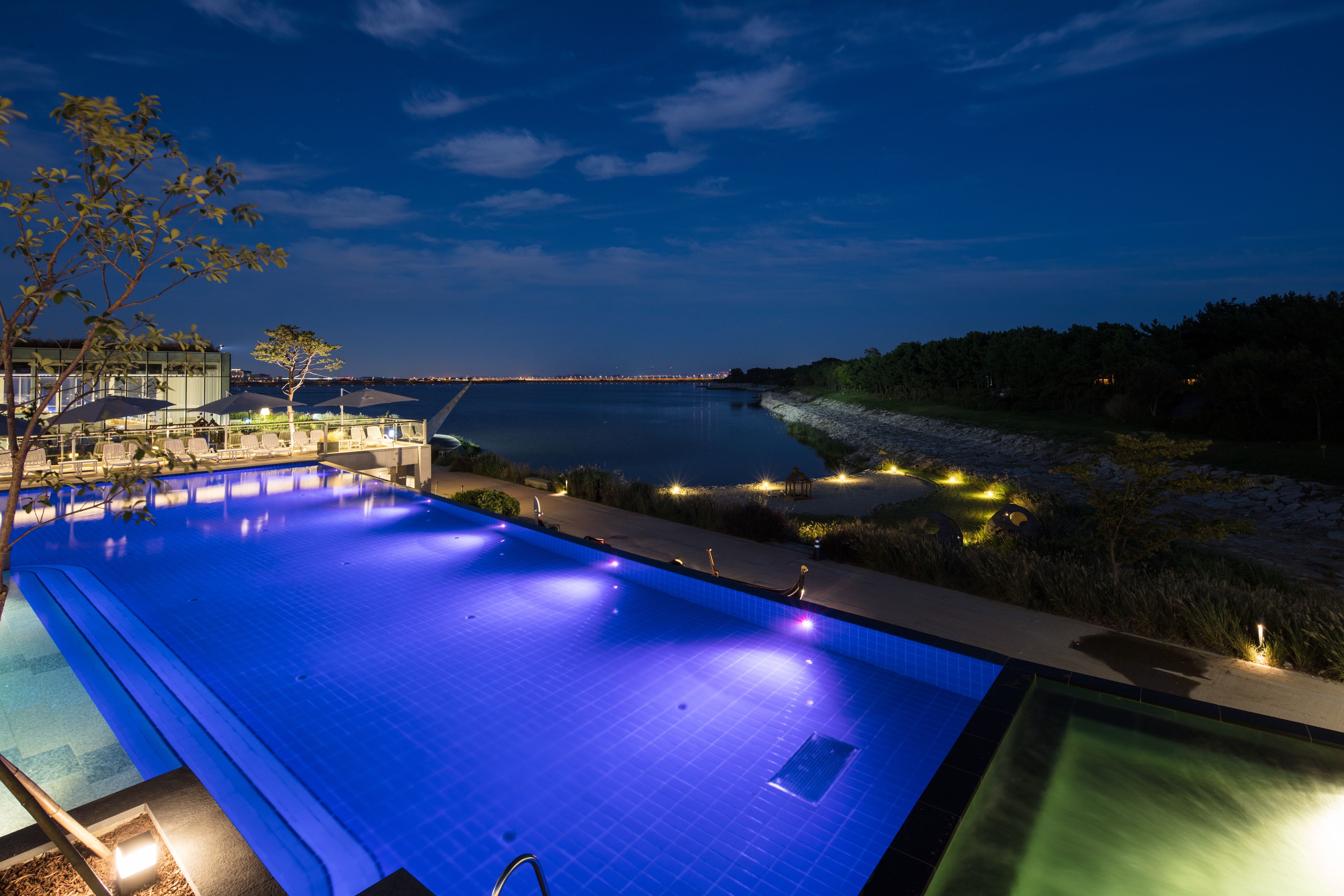 A large outdoor swimming pool with a view of the water and a distant cityscape at night.