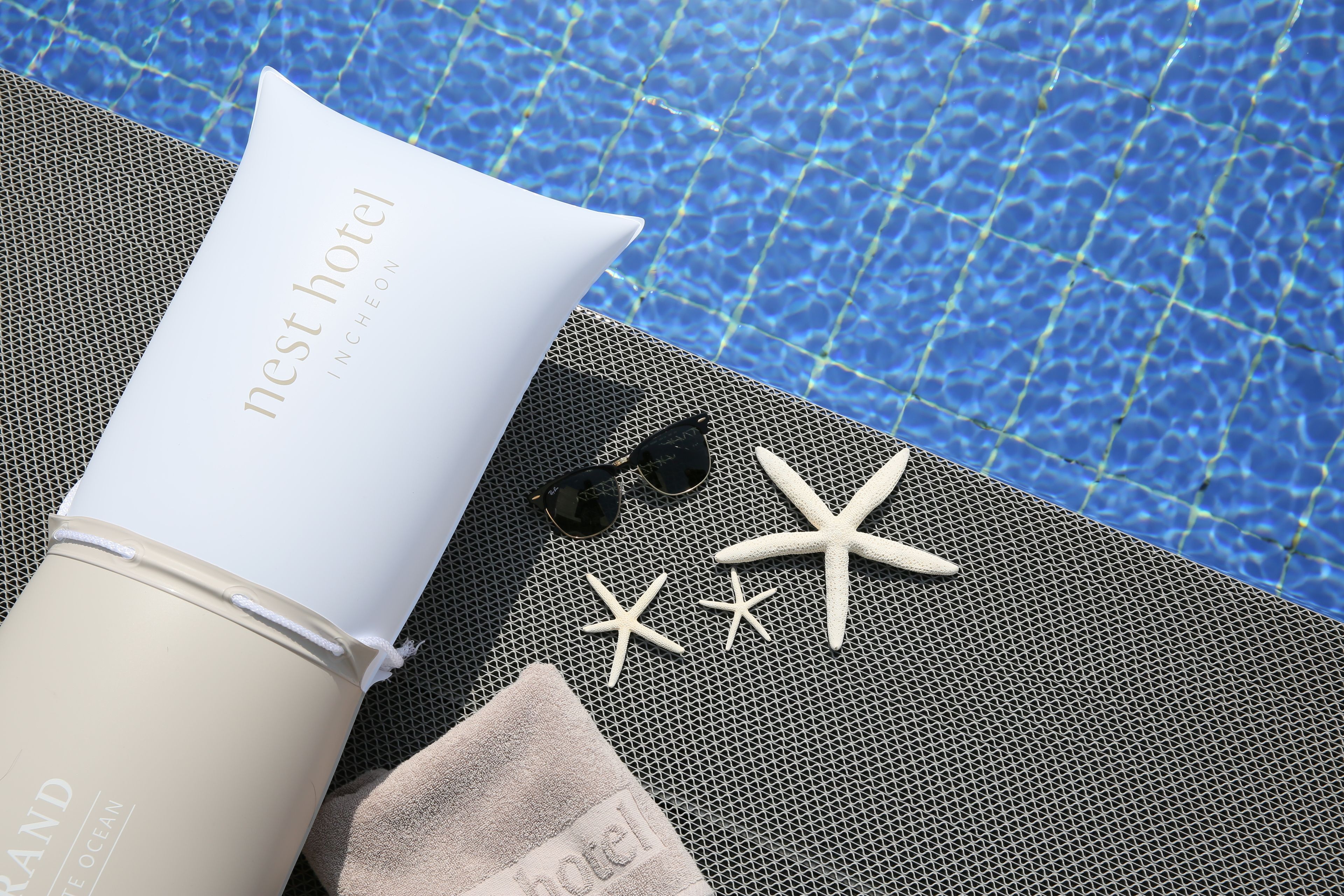 A beach towel, a bottle, sunglasses, and starfish by a pool.