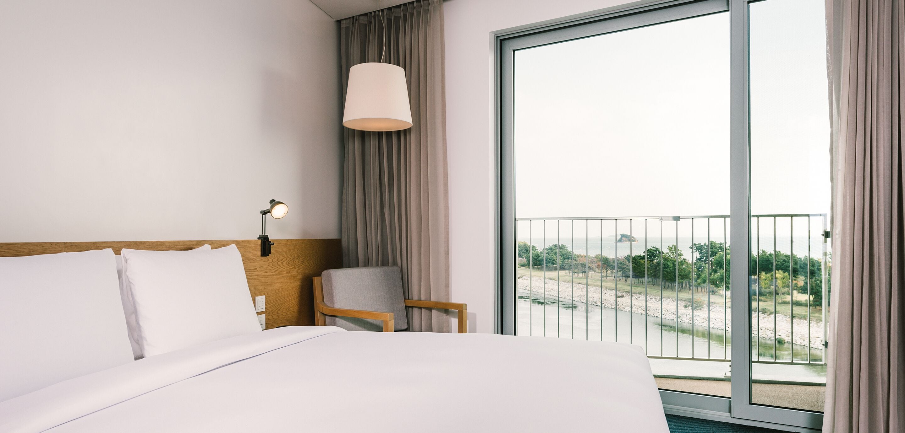 Ein Hotelzimmer mit einem großen Bett, einem Sessel, einem Schreibtisch, einer Lampe und einem Balkon mit Landschaftsblick.