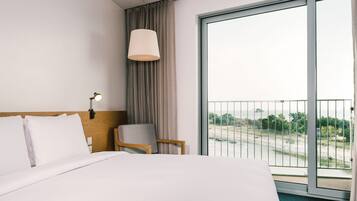Ein Hotelzimmer mit einem großen Bett, einem Sessel, einem Schreibtisch, einer Lampe und einem Balkon mit Landschaftsblick.