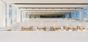 A modern restaurant with a spacious interior, featuring high ceilings, large windows, and a clean, minimalist design.