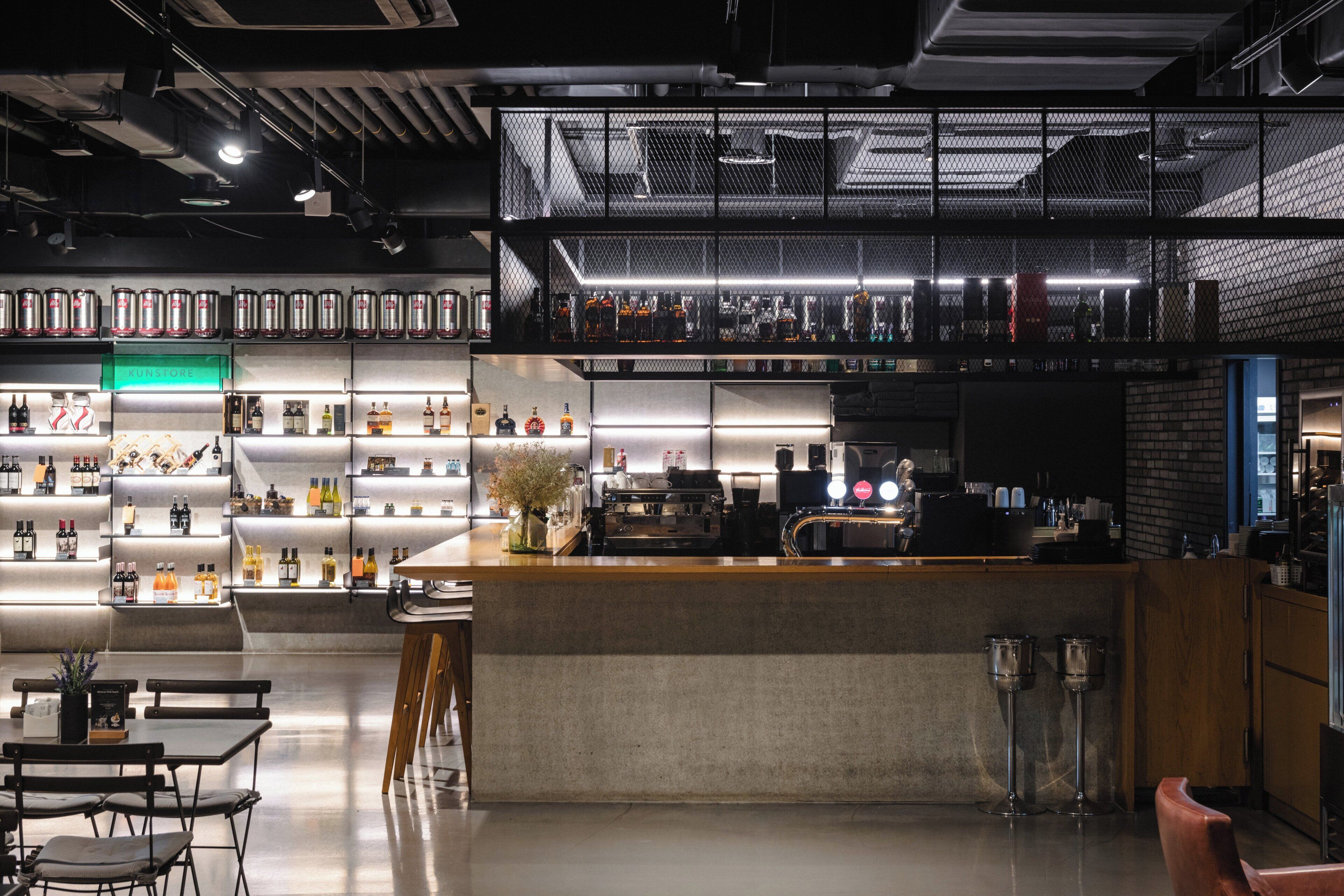 A modern bar area with a high counter, shelves with bottles, and a coffee machine.