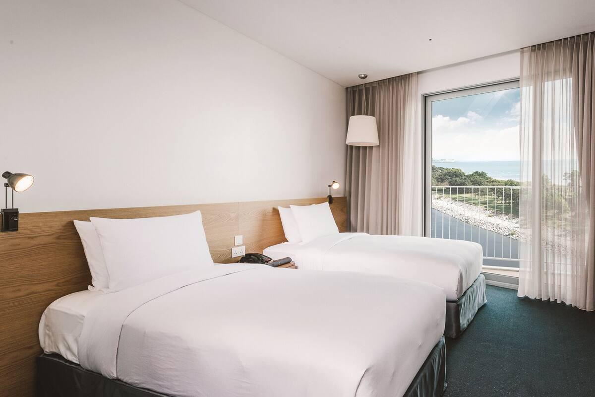 A hotel room with two beds, a large window with a view, a flat-screen TV, and a small table.