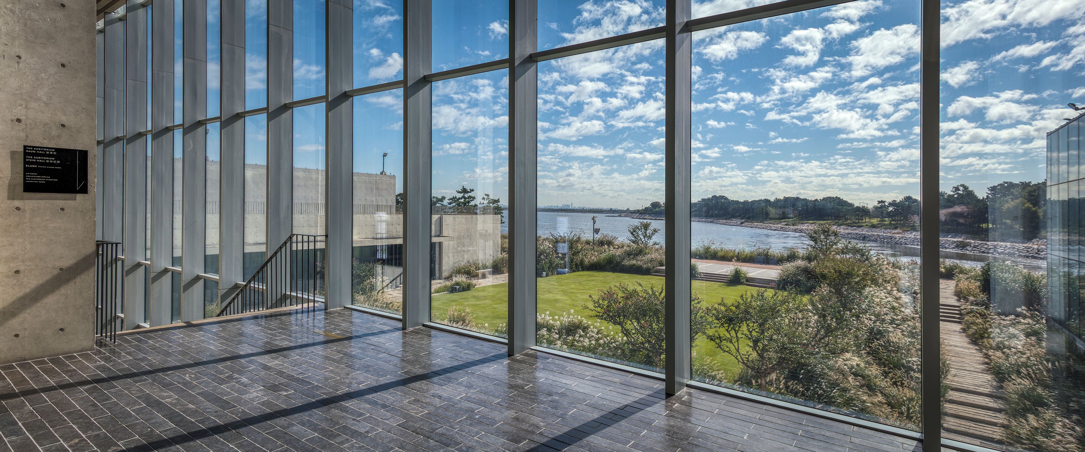 A modern building with large windows offering a view of a river and greenery.