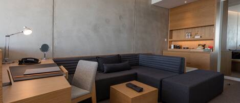 Una habitación de hotel moderna con un sofá modular, un escritorio con lámpara, un teléfono y una mesita.