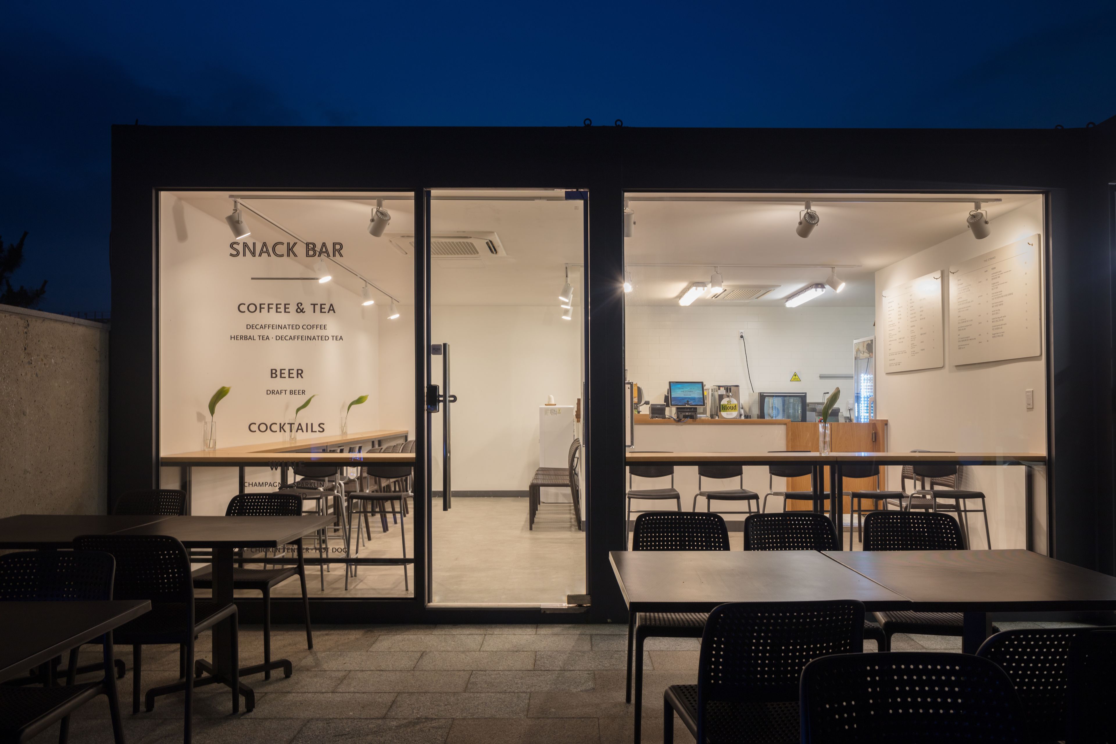 An indoor snack bar with tables and chairs, a menu board, and a counter with a computer.