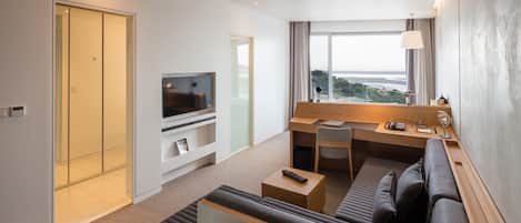 A hotel room with a TV, a desk with a lamp, a sofa, and a view of the outdoors.