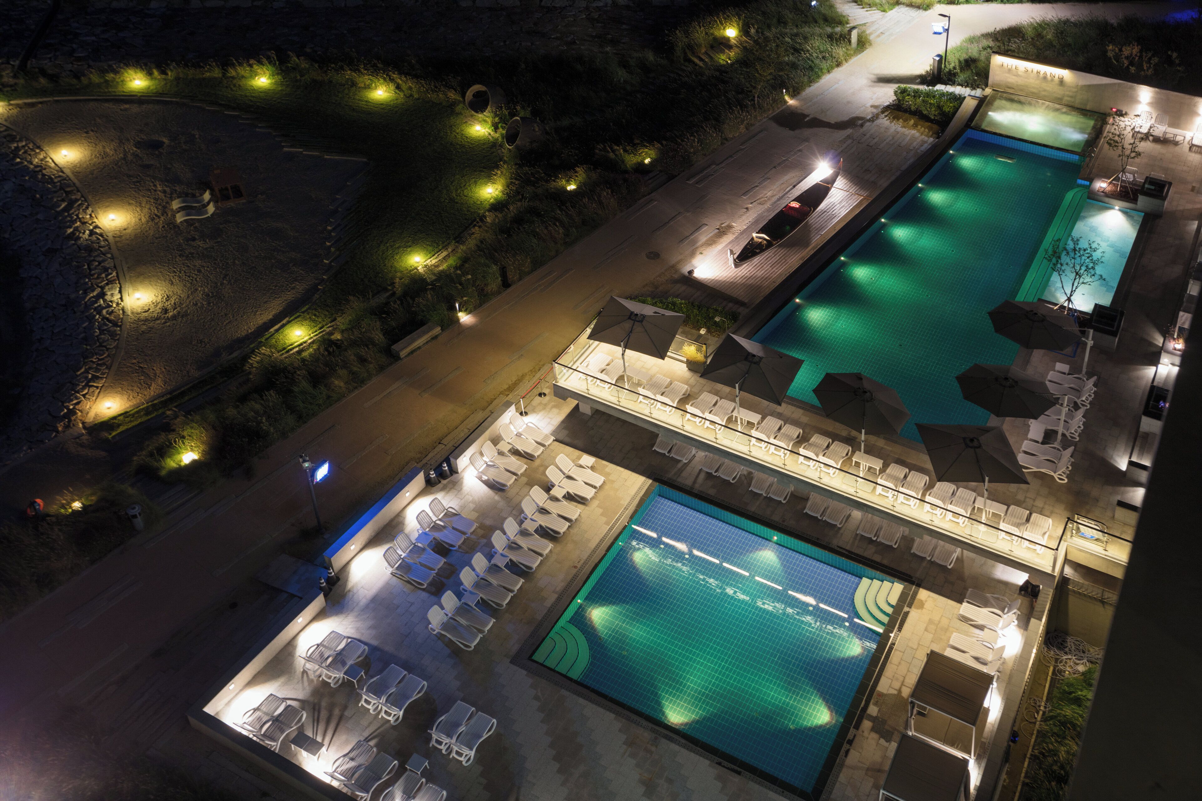 An aerial view of a hotel with two swimming pools, sun loungers, and a covered seating area.