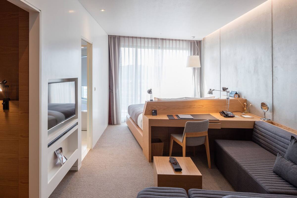 A modern hotel room with a bed, a desk, a sofa, and a TV.