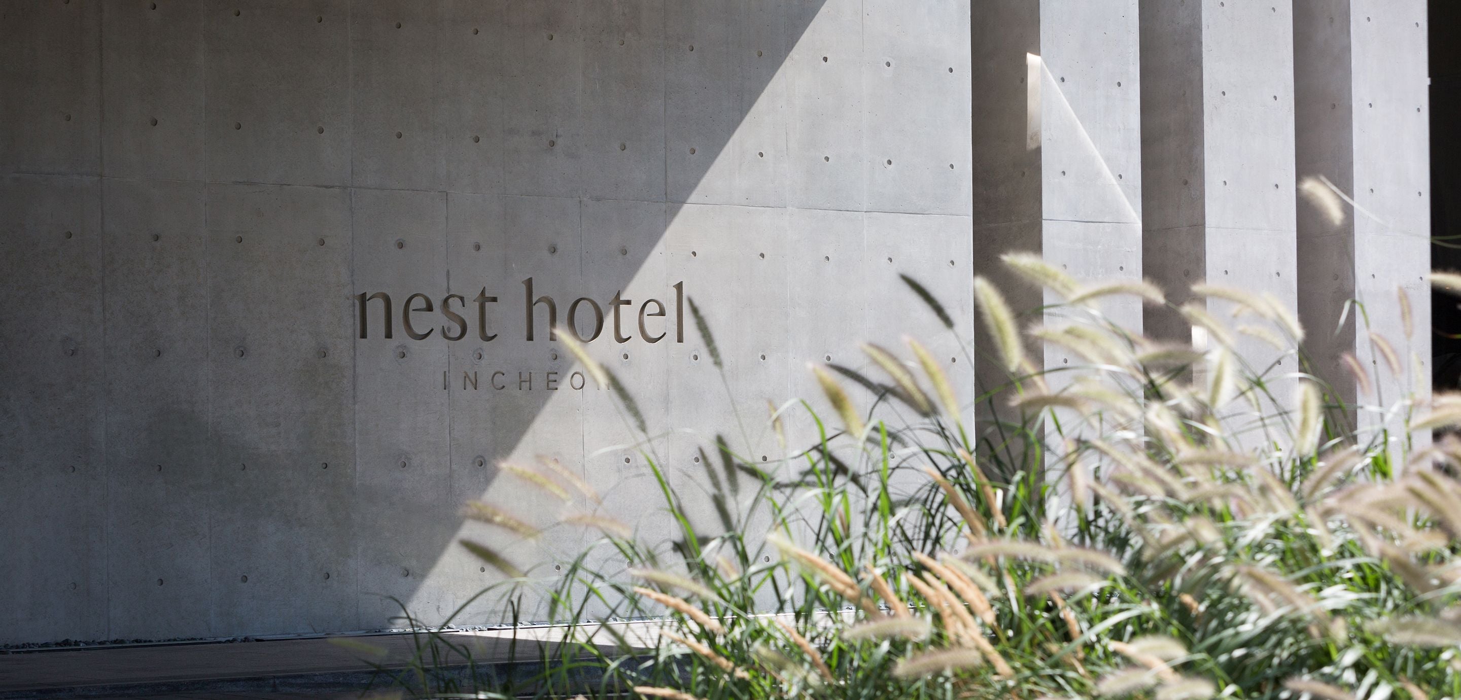 Eine Betonwand mit dem Schriftzug "nest hotel" und "INCHEO", die den Namen und Standort des Hotels angibt.