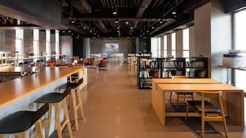 A modern library with a long wooden table, several chairs, and bookshelves.
