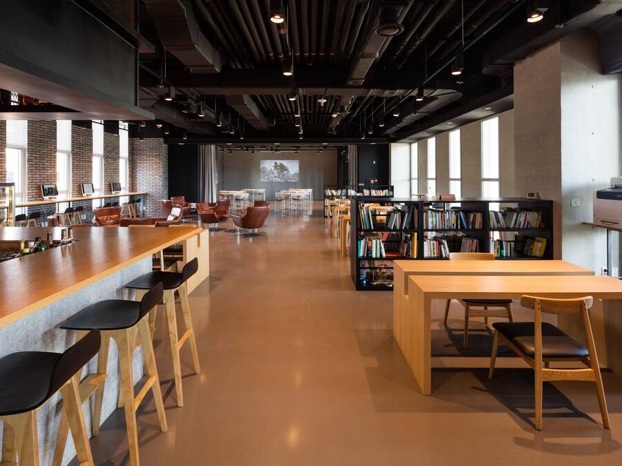 A modern library with a long wooden table, several chairs, and bookshelves.