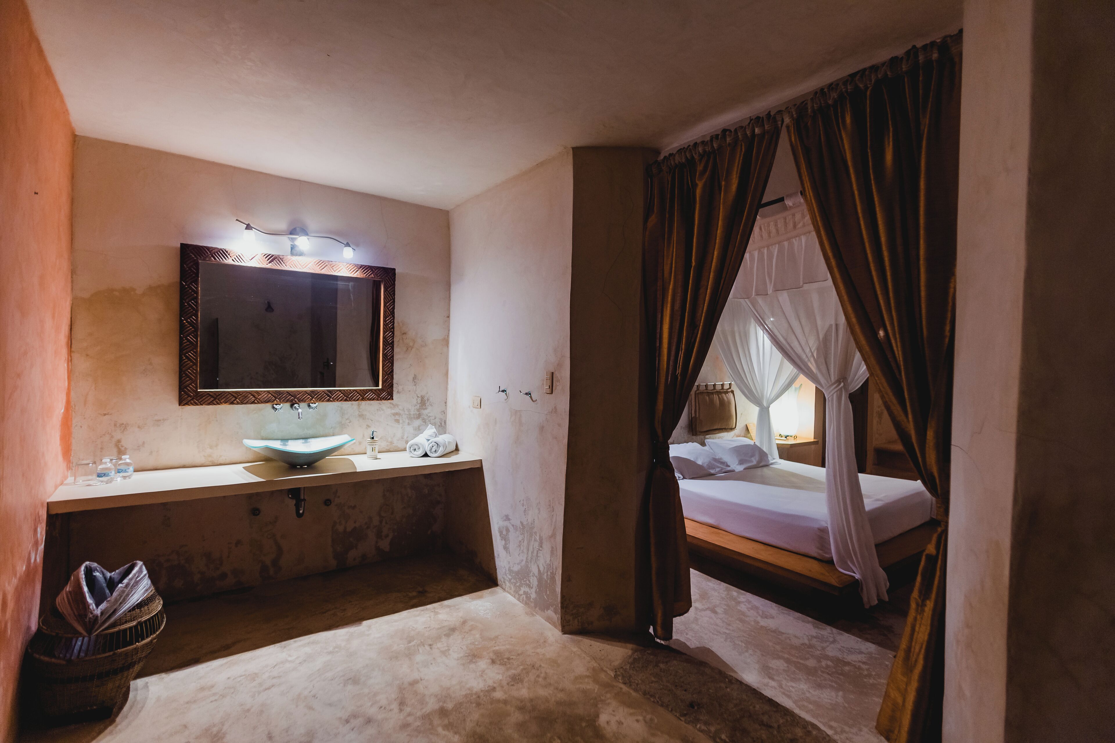 A room with a bed, a bedside table, a mirror, and a window with curtains.
