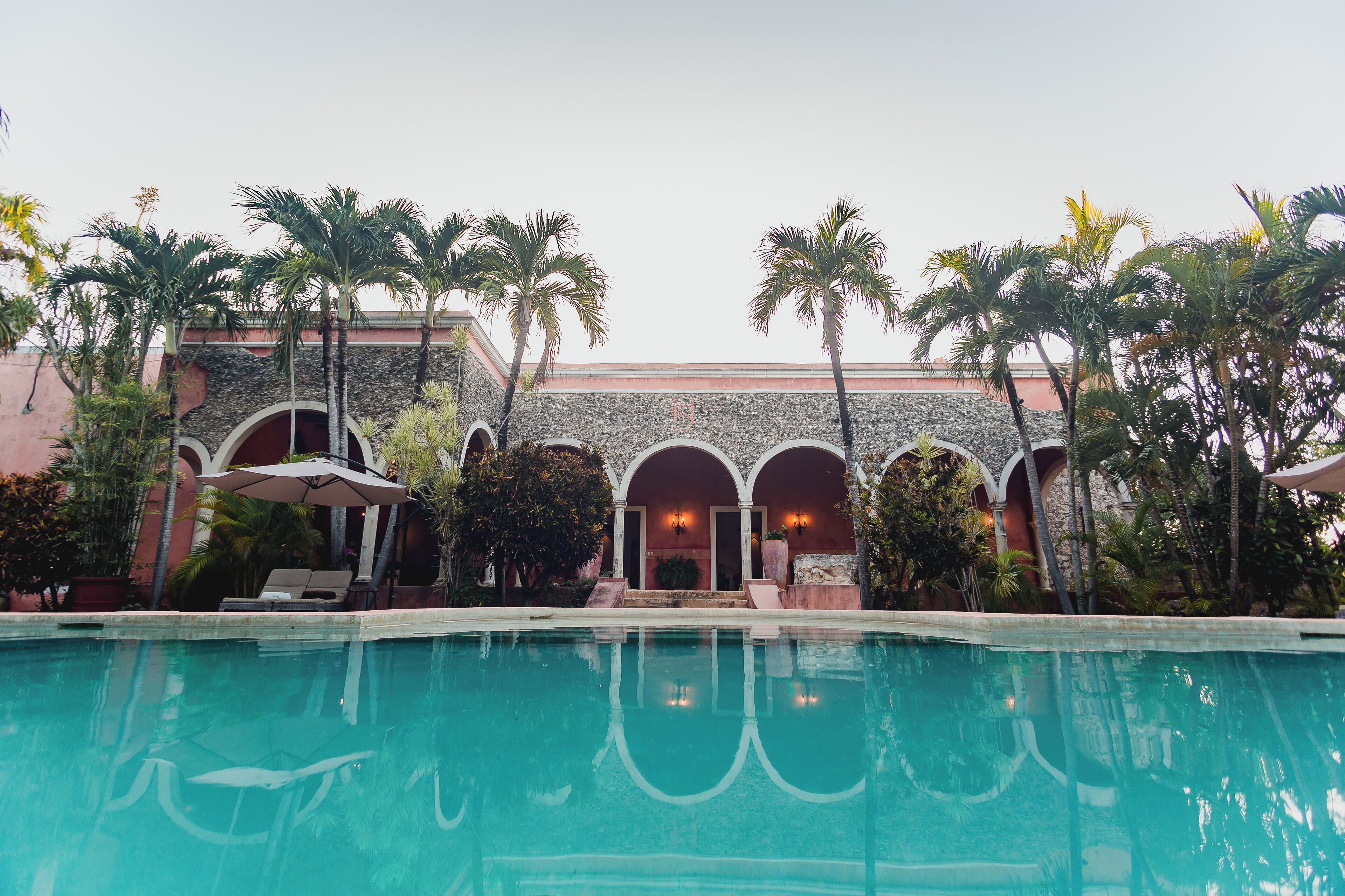 A pool area with a building in the background, surrounded by palm trees.