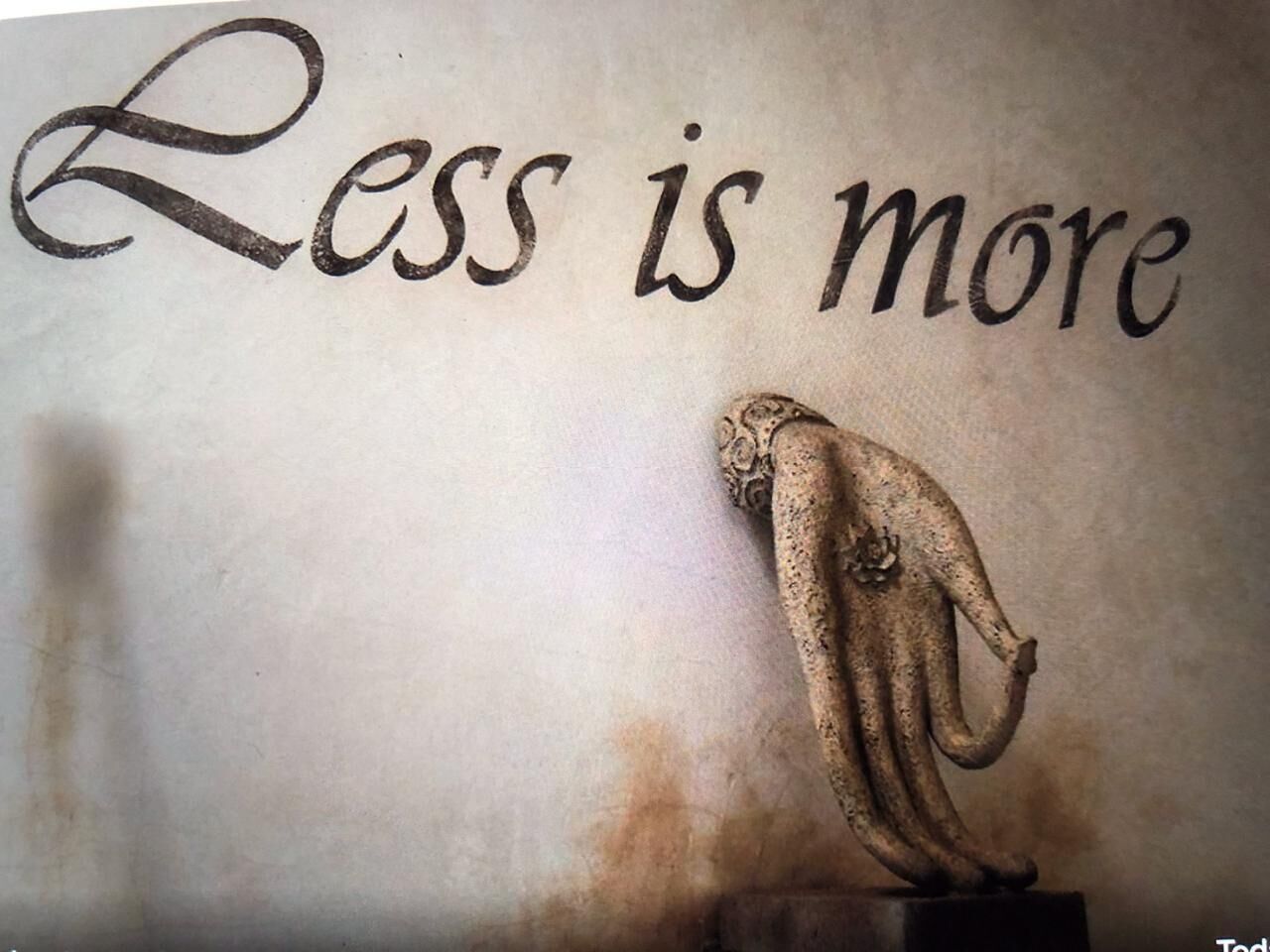 A wall with the phrase "Less is more" and a sculpture of a hand.