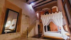 Una habitación con cama con dosel, un espejo grande y una escalera que lleva a un nivel superior.