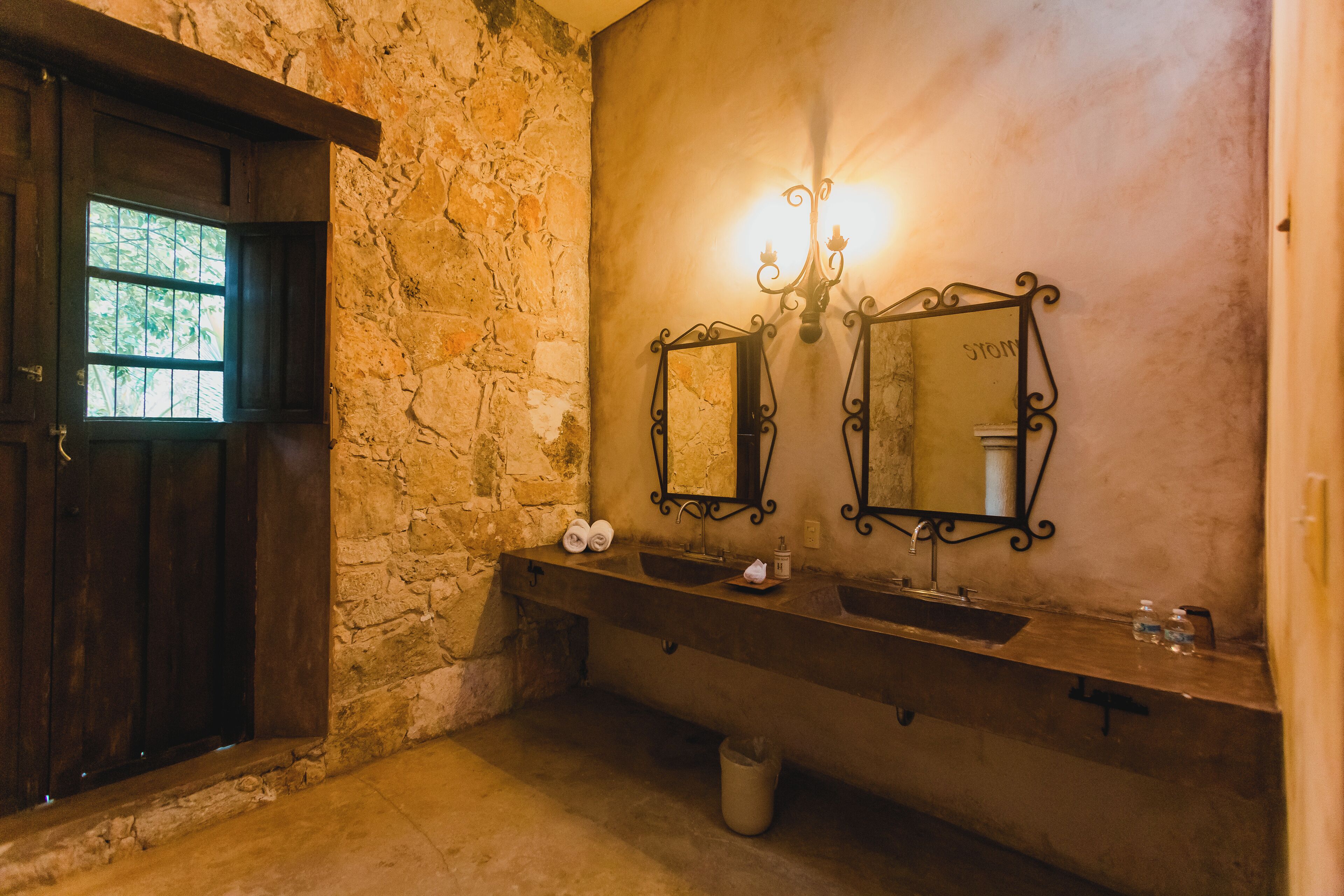 Un baño rústico con paredes de piedra, una puerta de madera y dos lavamanos con espejos.