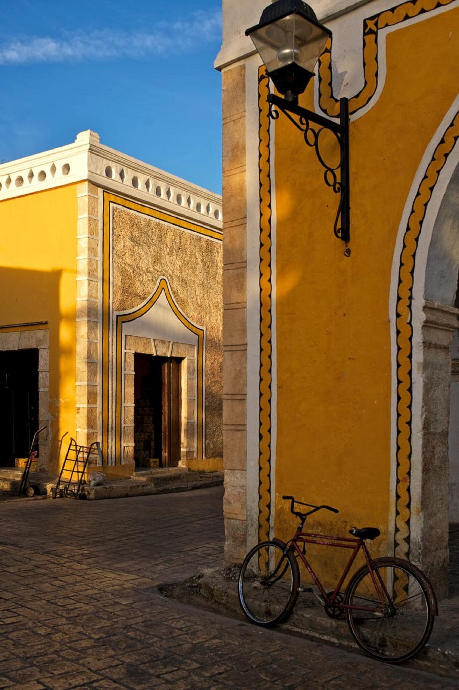 A cobblestone street with a yellow building featuring a large archway and a bicycle parked in front.