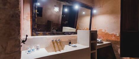 A bathroom with a large mirror, a sink with multiple faucets, and a shelf with toiletries.