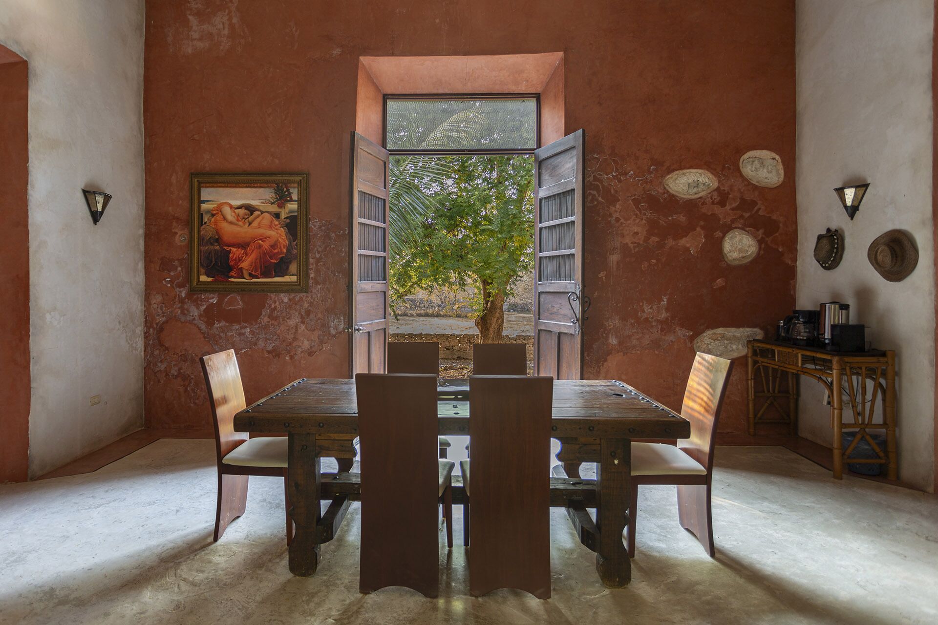 Un comedor con una mesa y sillas de madera, un cuadro en la pared y vistas a través de una puerta abierta.