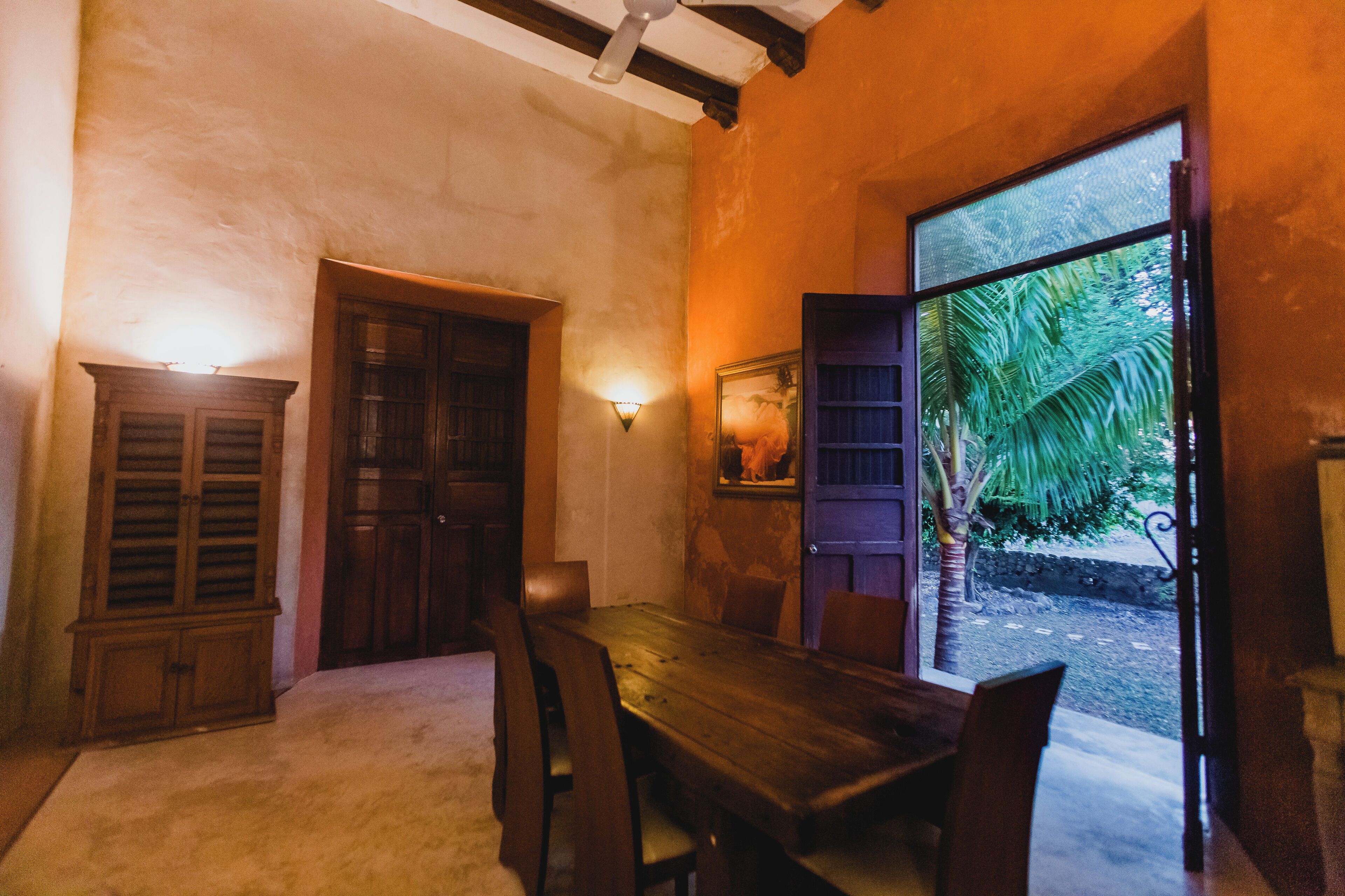 A dining area with a wooden table and chairs, a wooden cabinet, and a wall-mounted light fixture.