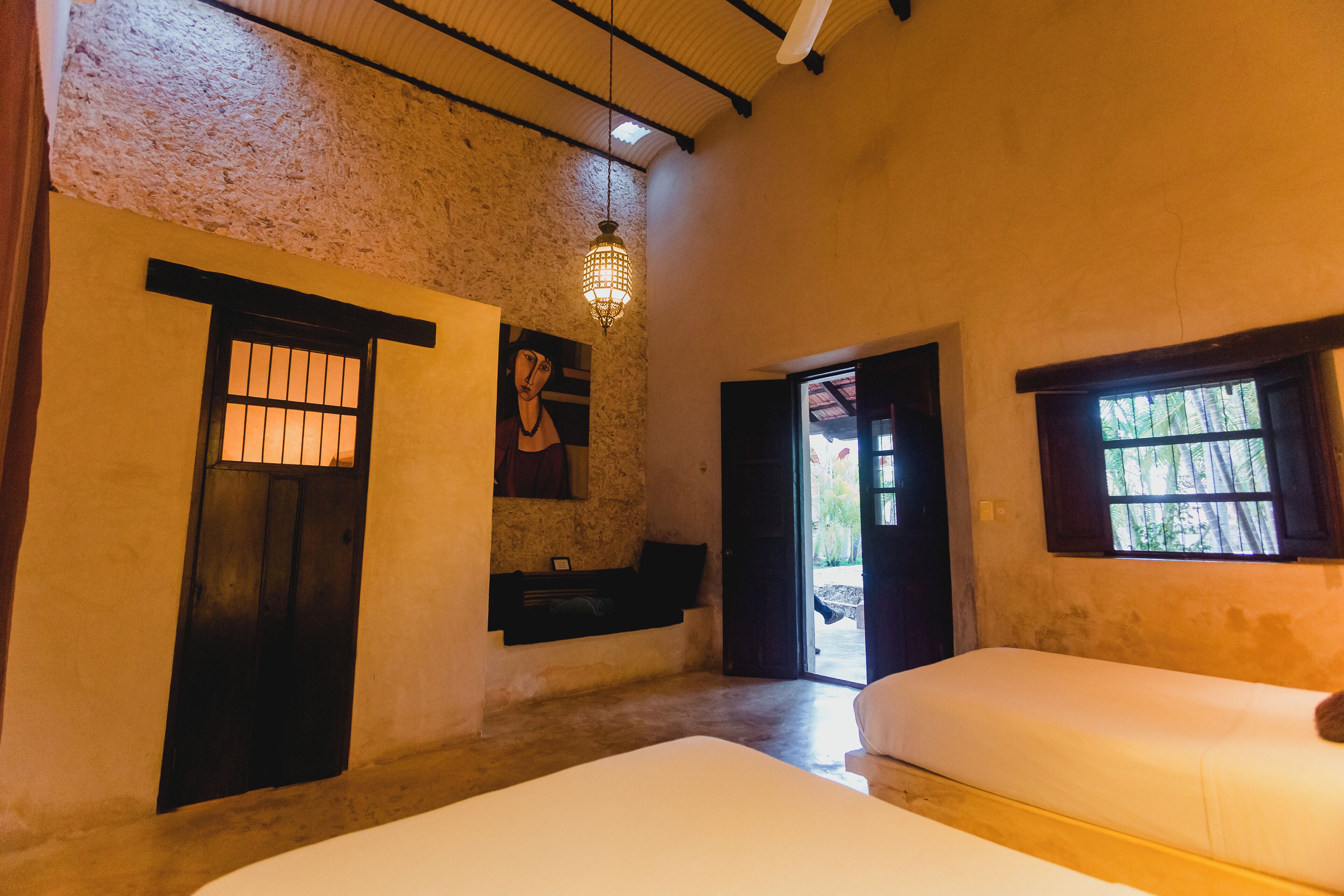 Une chambre avec deux lits, un mur en pierre, un luminaire suspendu et une fenêtre donnant sur un beau paysage.