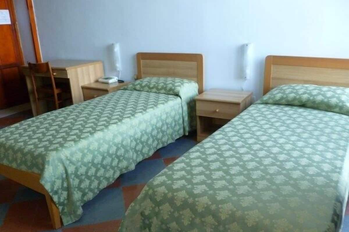 Een kamer met twee eenpersoonsbedden, elk met een houten frame en beddengoed met een groen patroon. Er staan nachtkastjes met lampen en een klein tafeltje met een stoel.