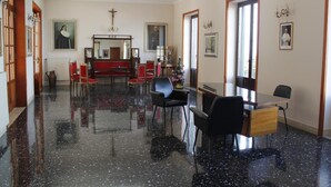 Une pièce spacieuse dotée d’un plancher noir poli, d’un bureau en bois avec des chaises, d’un canapé rouge et d’un grand miroir.