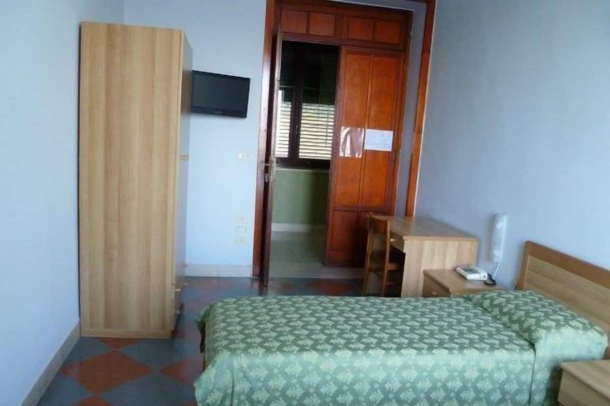 Een kamer met een bed, een bureau, een kledingkast en een televisie aan de muur.