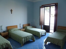 Una habitación con cuatro camas, una cruz en la pared y una ventana con vistas.
